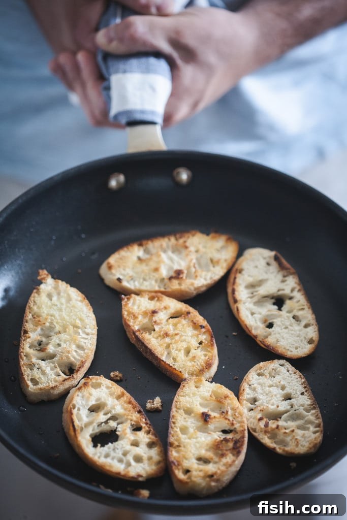 Crostini Quartet: Four Party-Ready Bites 5 Close-up view of baguette slices toasting in a non-stick frying pan, glistening with olive oil.