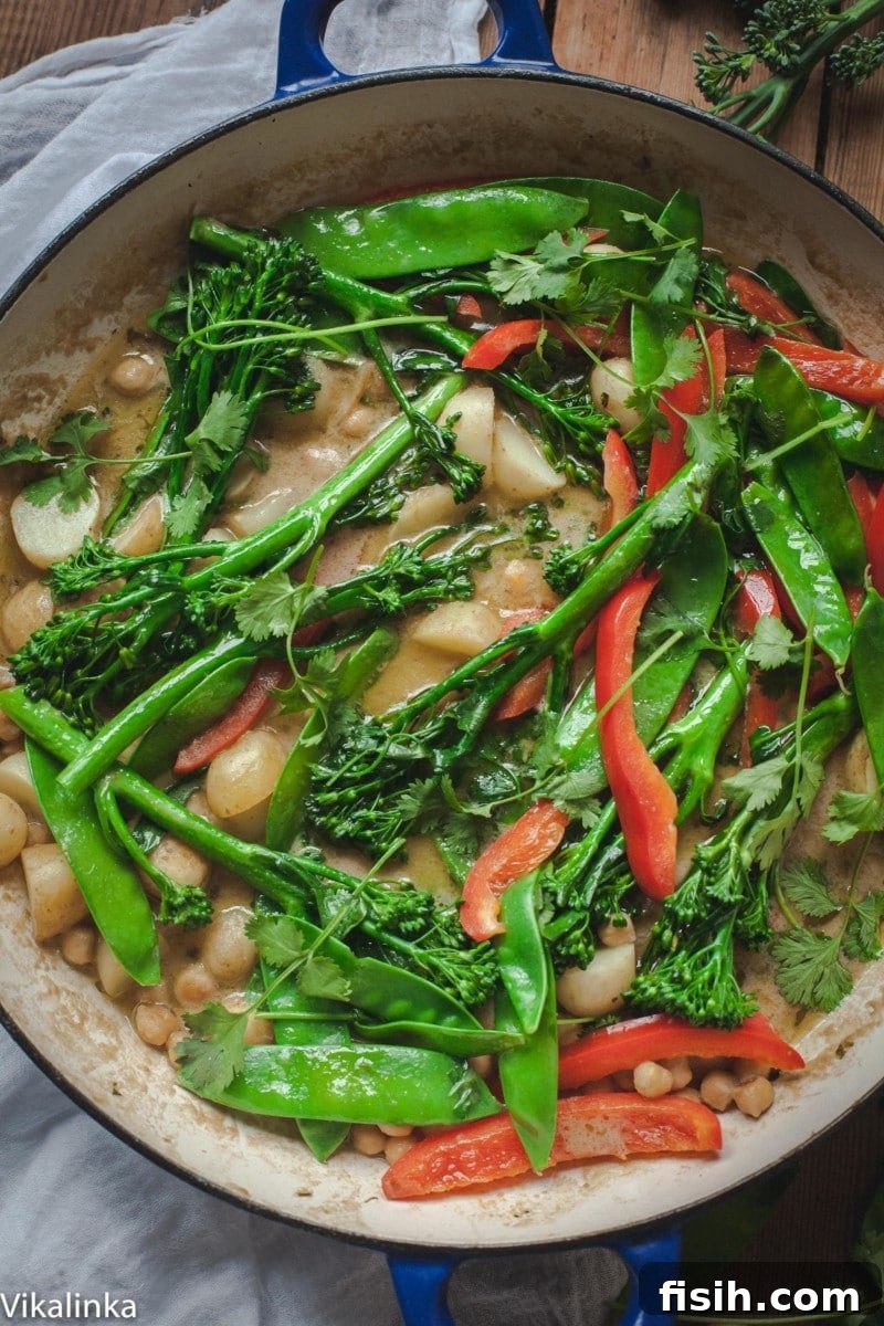 Overhead shot of Vegetarian Thai Green Curry in a wok, with a serving spoon and fresh ingredients.