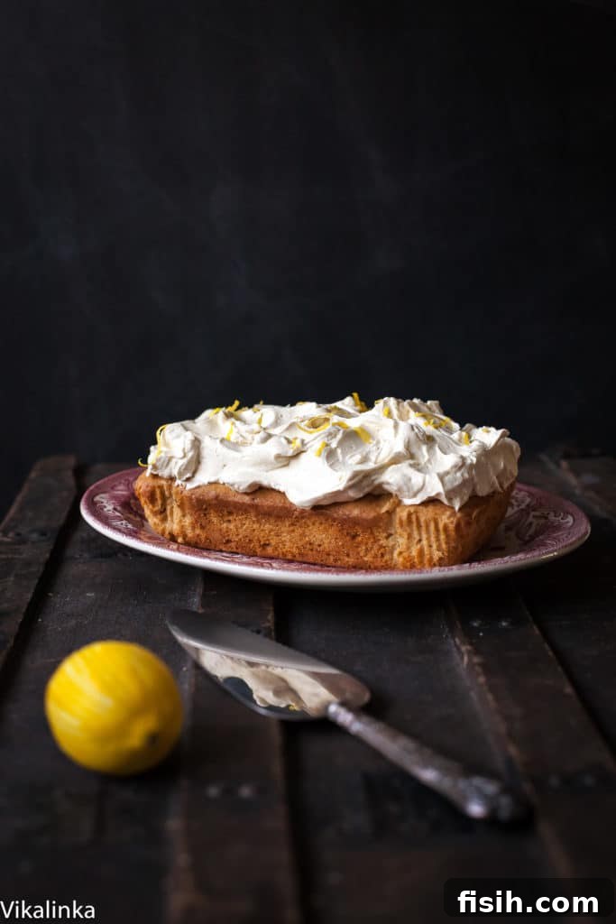 Zesty Lemon Ricotta Cloud Cake with Tangy Cream Cheese Frosting 5 A freshly sliced lemon ricotta cake with cream cheese frosting, presented beautifully on a cake platter next to a cake slicer and a fresh lemon, ready to be enjoyed.