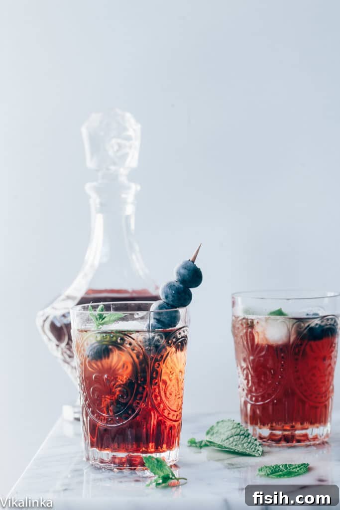 A close-up of the sparkling Vermouth Cassis cocktail garnished with blueberries and mint.