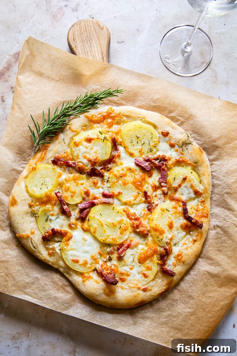 Close-up top-down view of a freshly baked pizza bianca, featuring golden potato slices, crispy pancetta, melted mozzarella, and smoked Gouda on a piece of parchment paper, resting on a wooden cutting board.