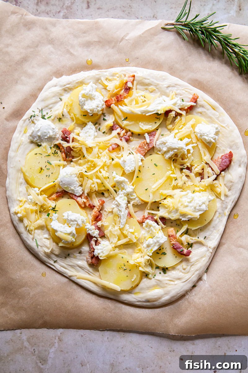 Unbaked potato and pancetta pizza showing the dough topped with potato slices, raw pancetta, mozzarella, and smoked Gouda, ready for the oven.
