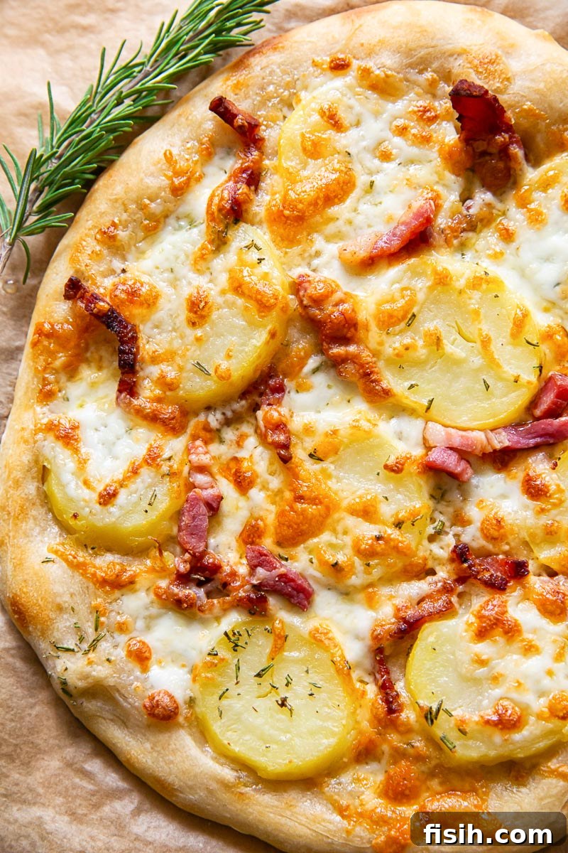 A freshly baked potato and pancetta pizza on parchment paper, alongside a sprig of fresh rosemary, emphasizing the rustic and aromatic qualities.