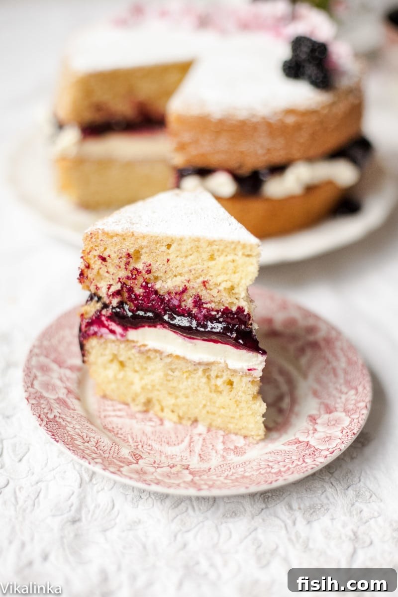 A close-up slice of Victoria Sponge Cake with a generous layer of mascarpone cream and blackberry compote, dusted with icing sugar