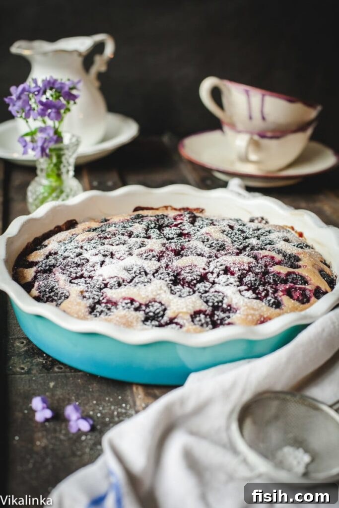 A delightful slice of Wild Blackberry Tea Cake on a plate, ready to be enjoyed with tea, with a blurred background of a cozy table setting.