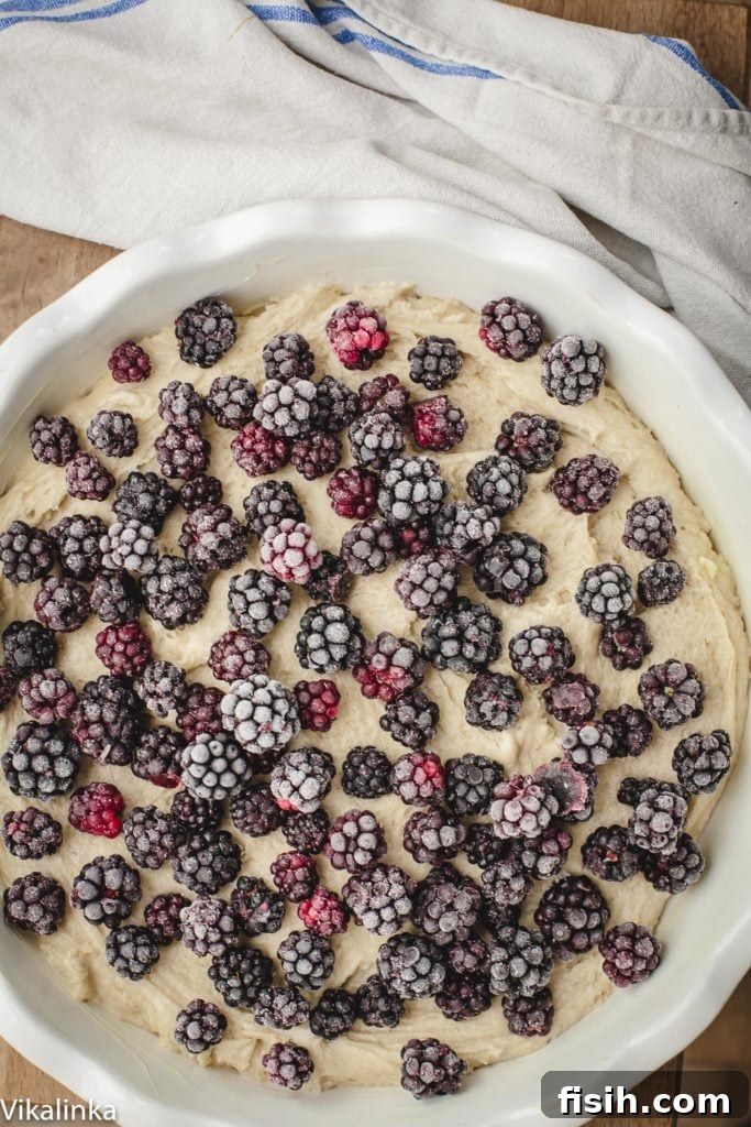 Unbaked cake batter in a baking dish, generously topped with an even layer of fresh blackberries, ready for the oven.