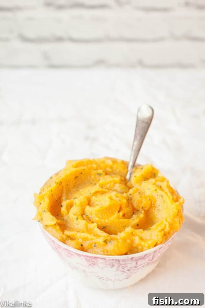 A close-up of creamy sweet potato and swede mash, garnished with fresh herbs, in a white bowl.