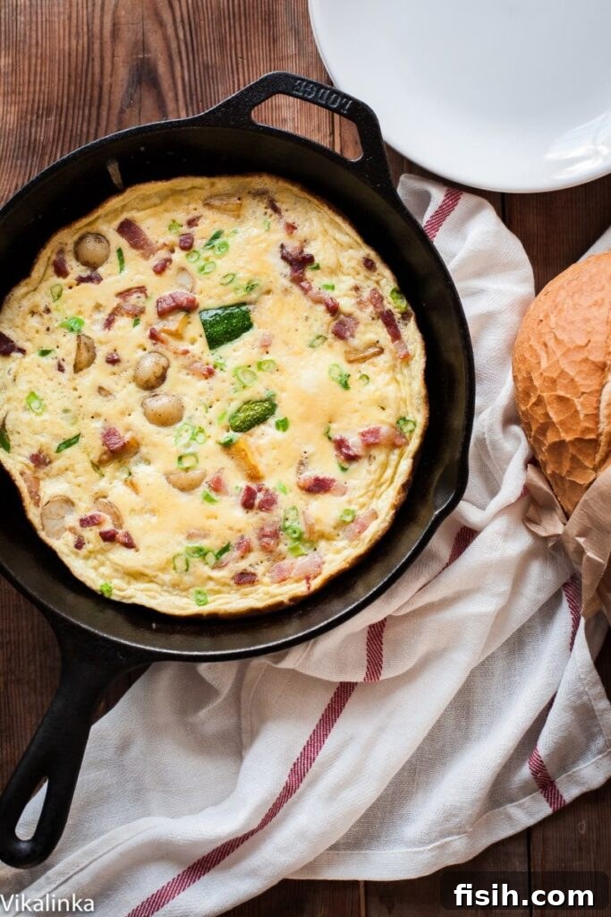 Golden French Omelette with Crispy Bacon, Roasted Potatoes, and Sautéed Zucchini, garnished with fresh herbs