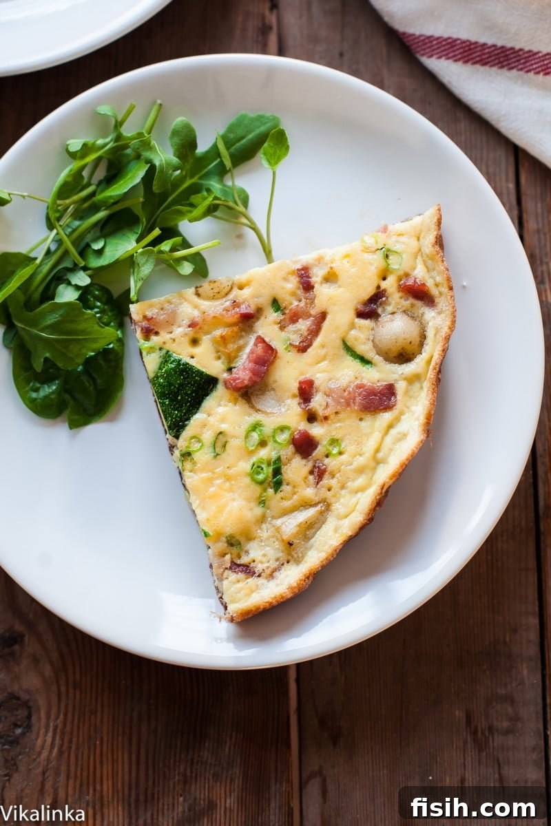 A slice of hearty French omelette with bacon, potatoes, and zucchini, served alongside a fresh green salad on a white plate