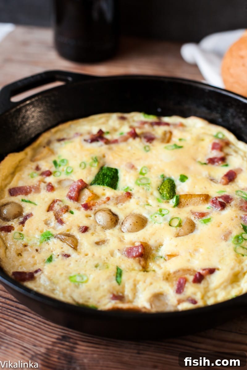 A cast iron pan holds a simmering omelette with visible pieces of bacon and potato, cooking to perfection