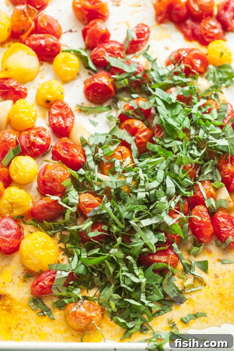 Roasted cherry tomatoes on a baking pan, ready to be mixed with fresh basil.