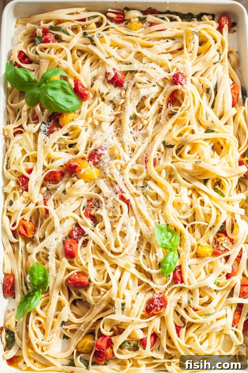Tagliatelle tossed with roasted cherry tomato and basil sauce on a rectangular serving pan.