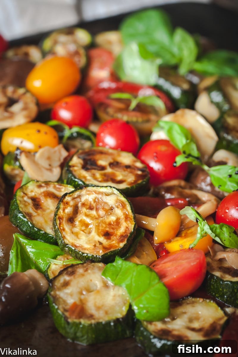 Close-up of warm zucchini salad with bright cherry tomatoes, red peppers, and basil leaves, glistening with vinaigrette.