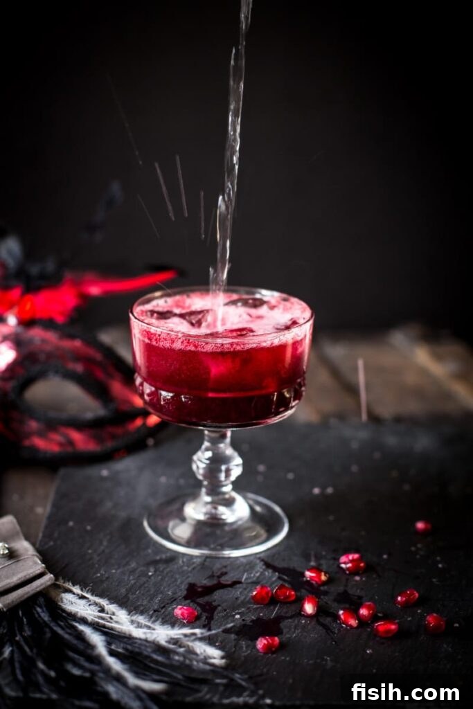 A vibrant red cocktail glass adorned with scattered pomegranate seeds, hinting at its refreshing and fruity contents.