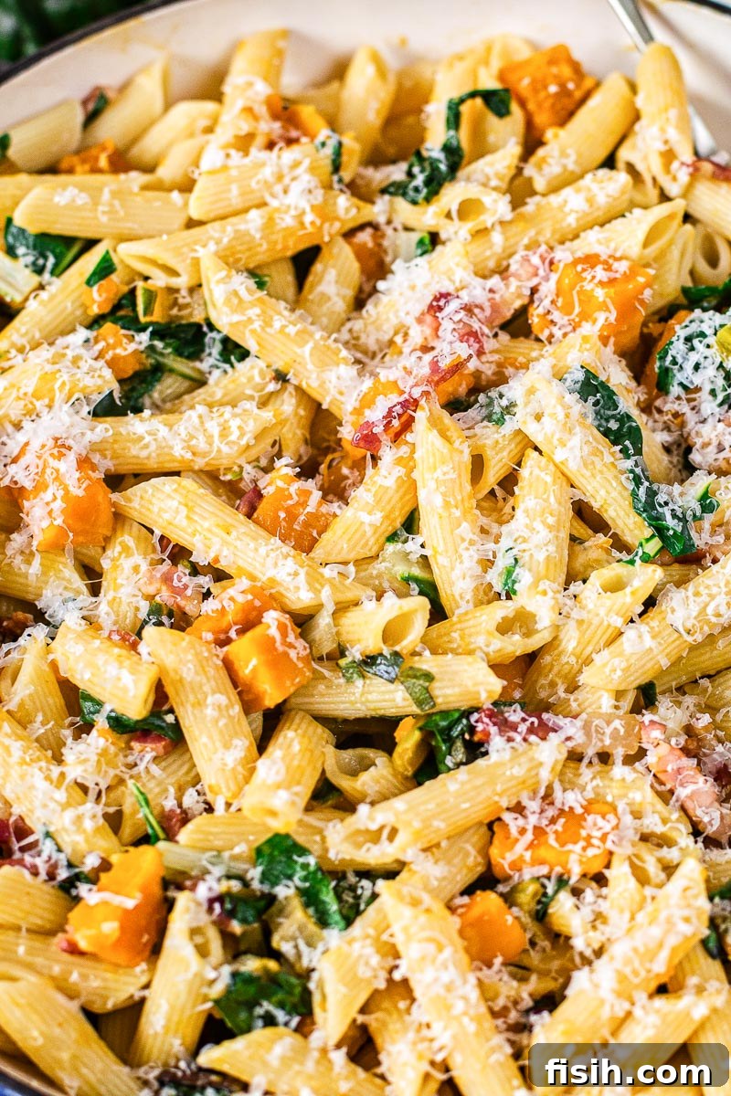 Close-up of penne pasta with roasted squash, pancetta, and Swiss chard, garnished with grated Parmesan cheese.