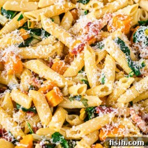 Penne pasta with roasted squash, pancetta, and Swiss chard sprinkled with Parmesan closeup