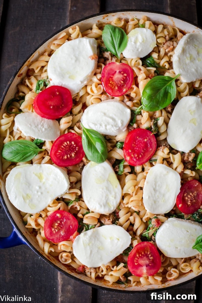 A close-up shot of baked fusilli pasta with sausage, vibrant arugula, and melted fresh mozzarella, showcasing the rich textures and colors of the dish.