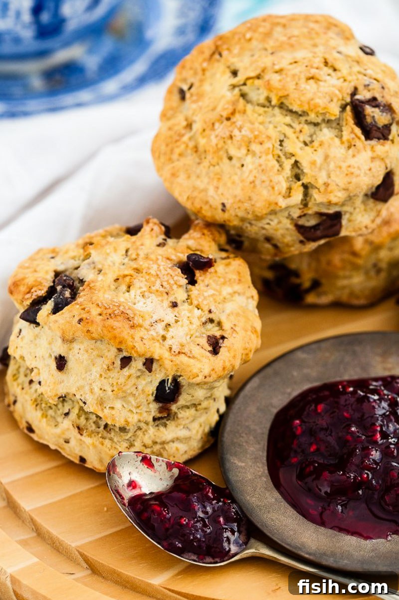 Two freshly baked chocolate chip scones, with a dollop of vibrant raspberry jam, presented on a wooden cutting board.