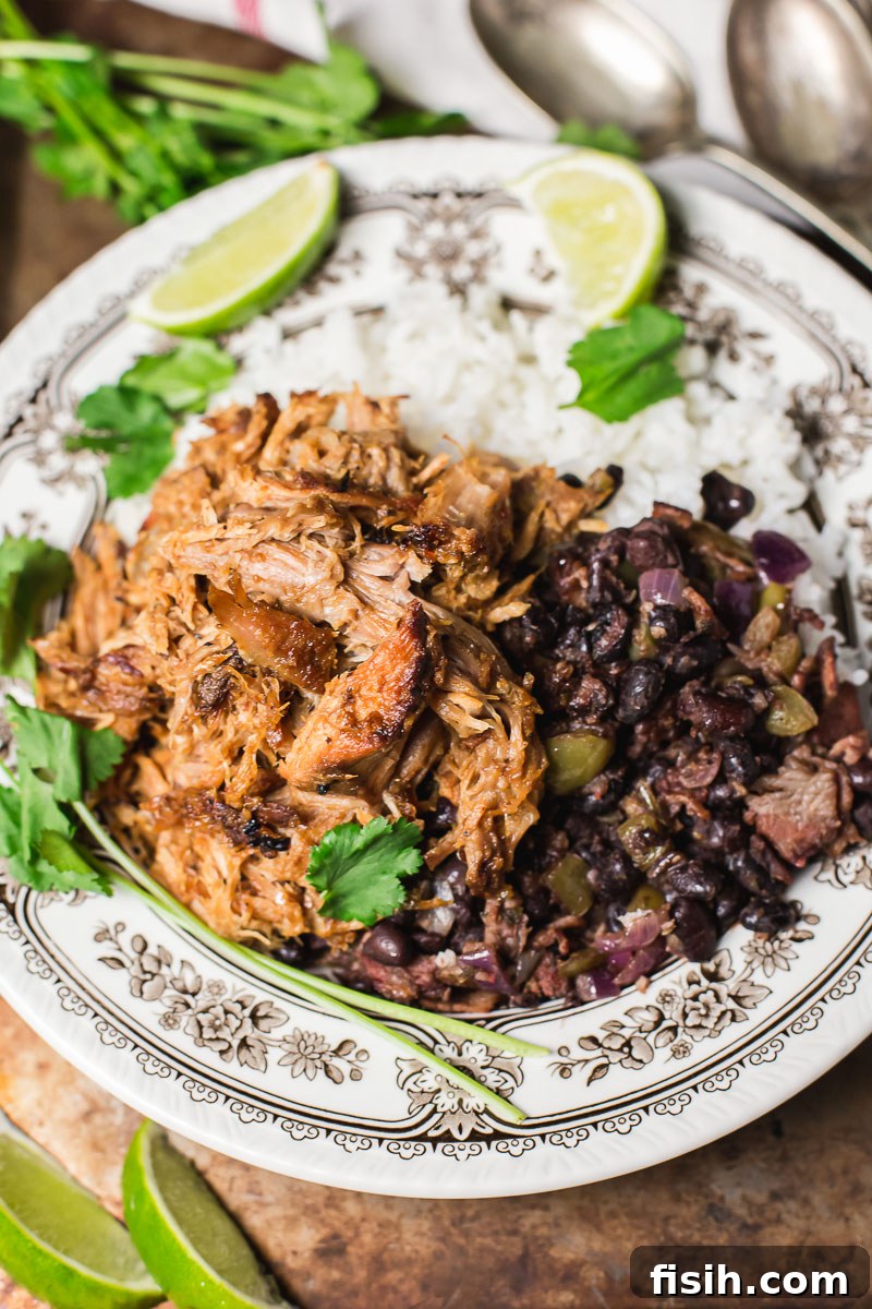 Tender, shredded Slow Cooker Cuban Pork (Lechon Asado) served with fluffy white rice, savory black beans, and fresh lime wedges.