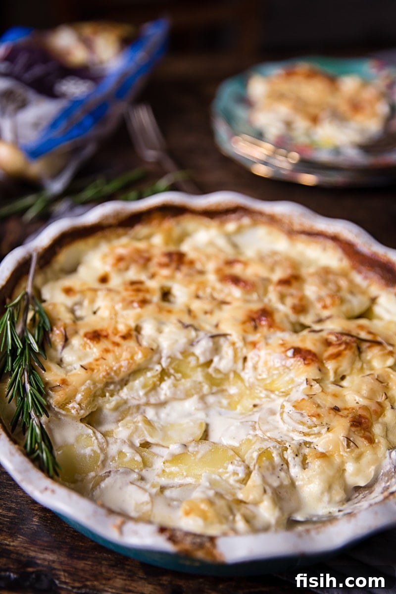Baking dish with rosemary potatoes au gratin and a spoonful removed, showing creamy layers