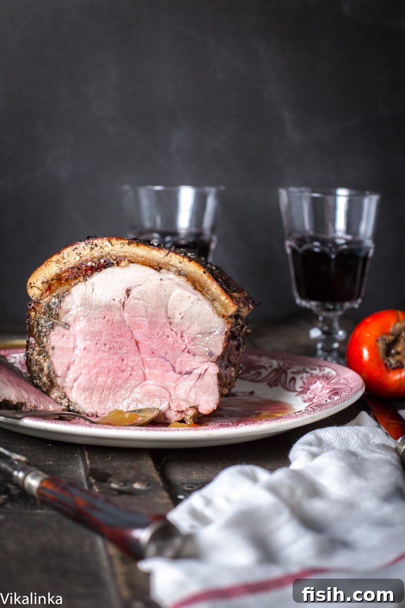 Sliced pork roast on a serving platter, with two glasses of red wine in the background