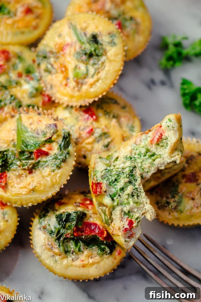 Freshly baked mini frittatas with vibrant vegetables held by a fork, showcasing its fluffy texture and colorful fillings.