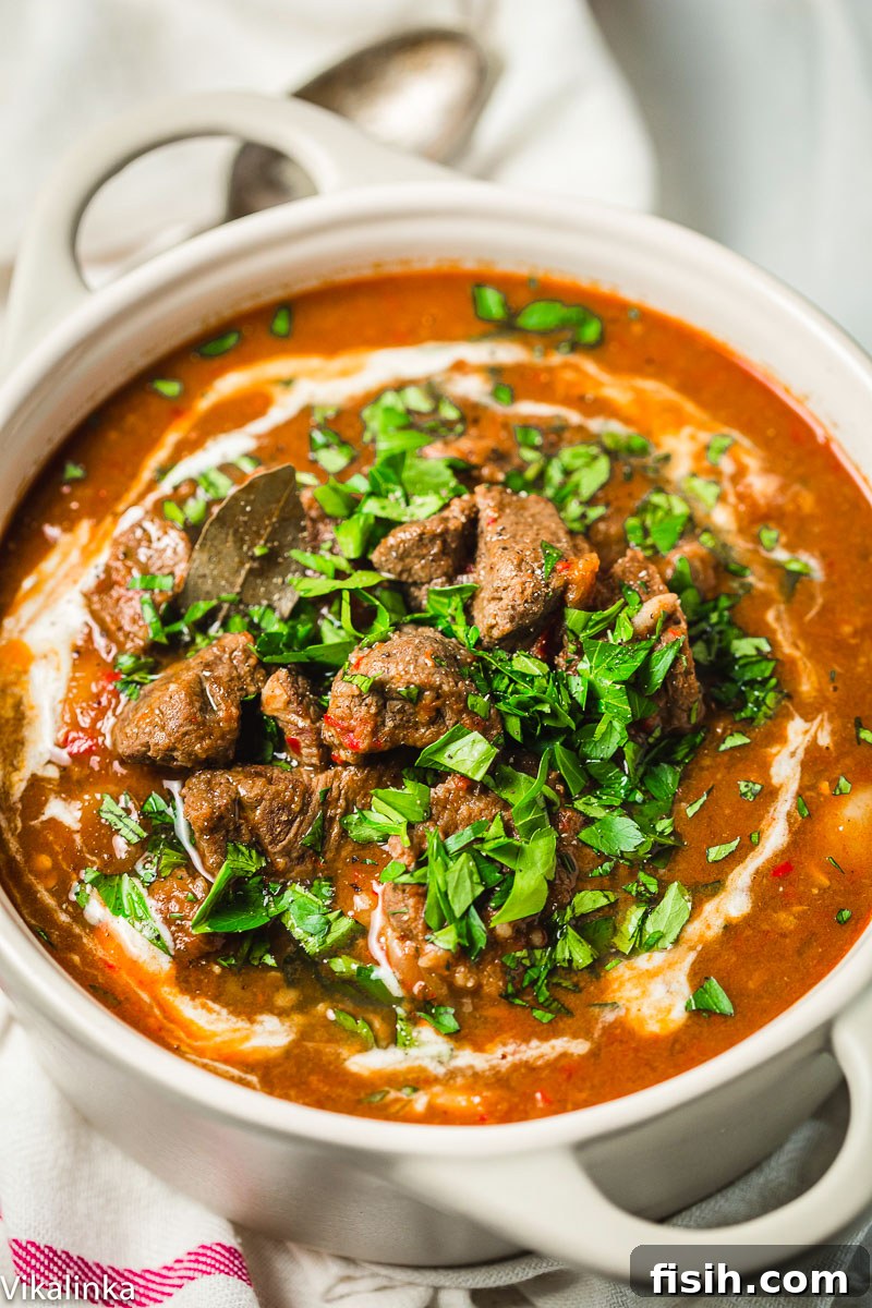 A close-up, top-down view of beef goulash in a deep pot, generously sprinkled with fresh, vibrant chopped parsley.