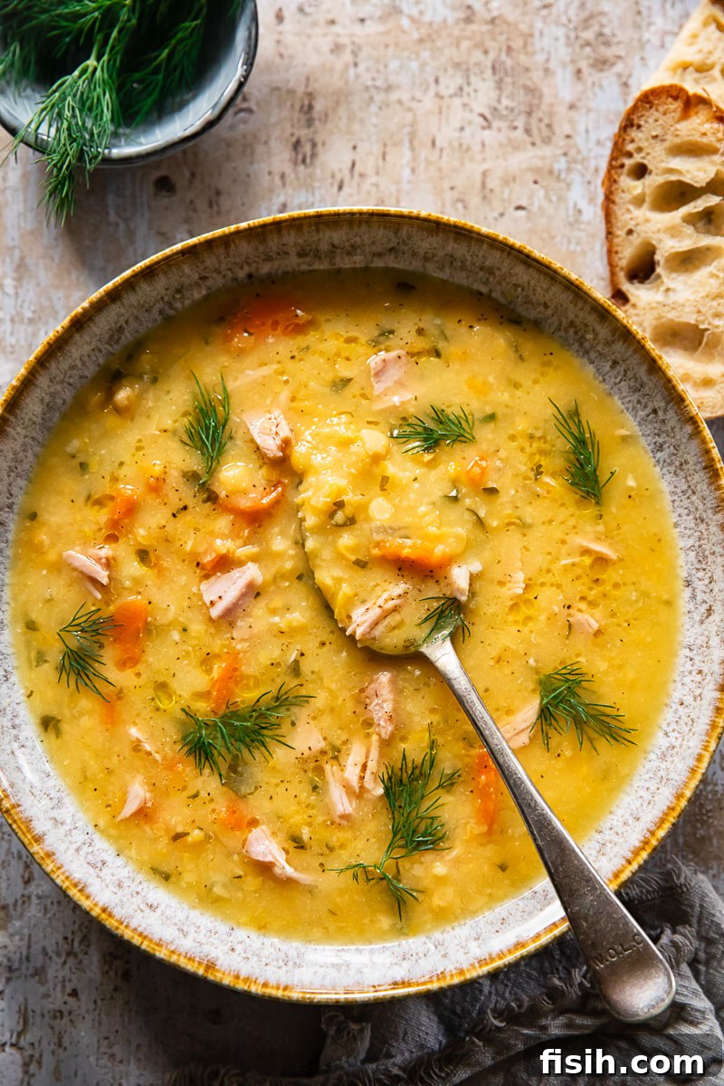 top down view of yellow split pea soup with ham and sprinkled with dil, a slice of bread near the bowl