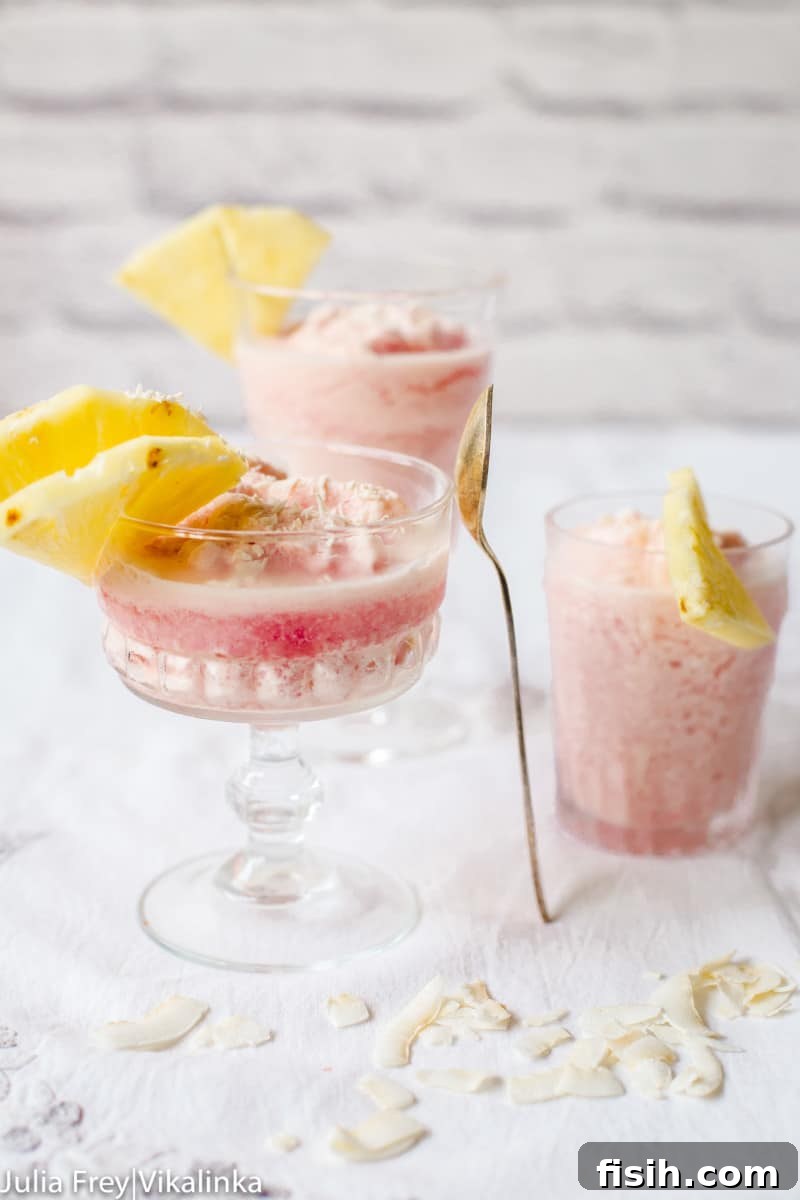 A vibrant frozen Blood Orange Piña Colada, beautifully garnished with fresh pineapple slices and a sprig of mint, ready to be enjoyed.