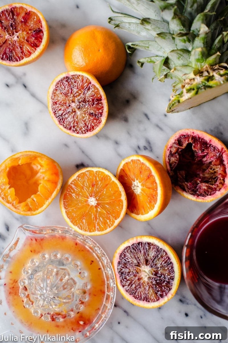 A still life showcasing the key ingredients: halved blood oranges and regular oranges, a glass of fresh juice, and a freshly cut pineapple, highlighting the natural goodness.