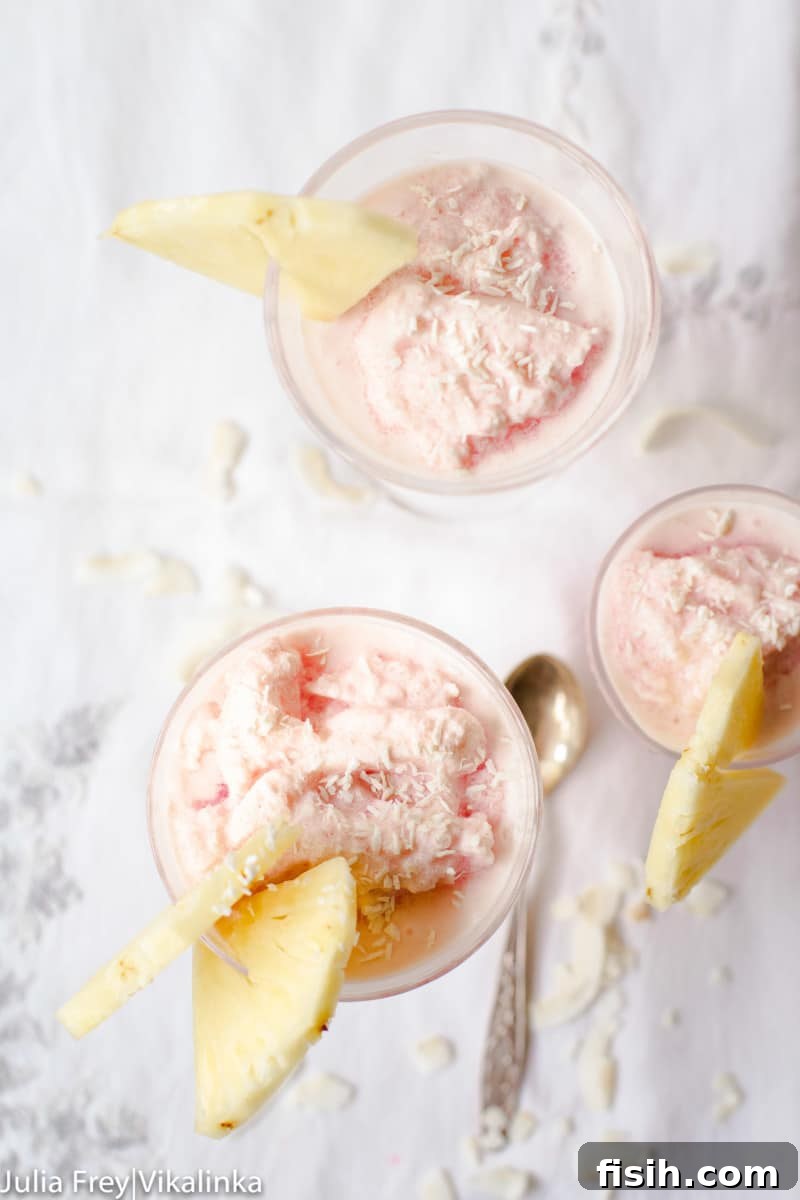 A top-down view of three elegant glasses, each filled with the exquisite frozen blood orange pina colada, adorned with fresh pineapple leaves and small fruit slices, creating a festive display.