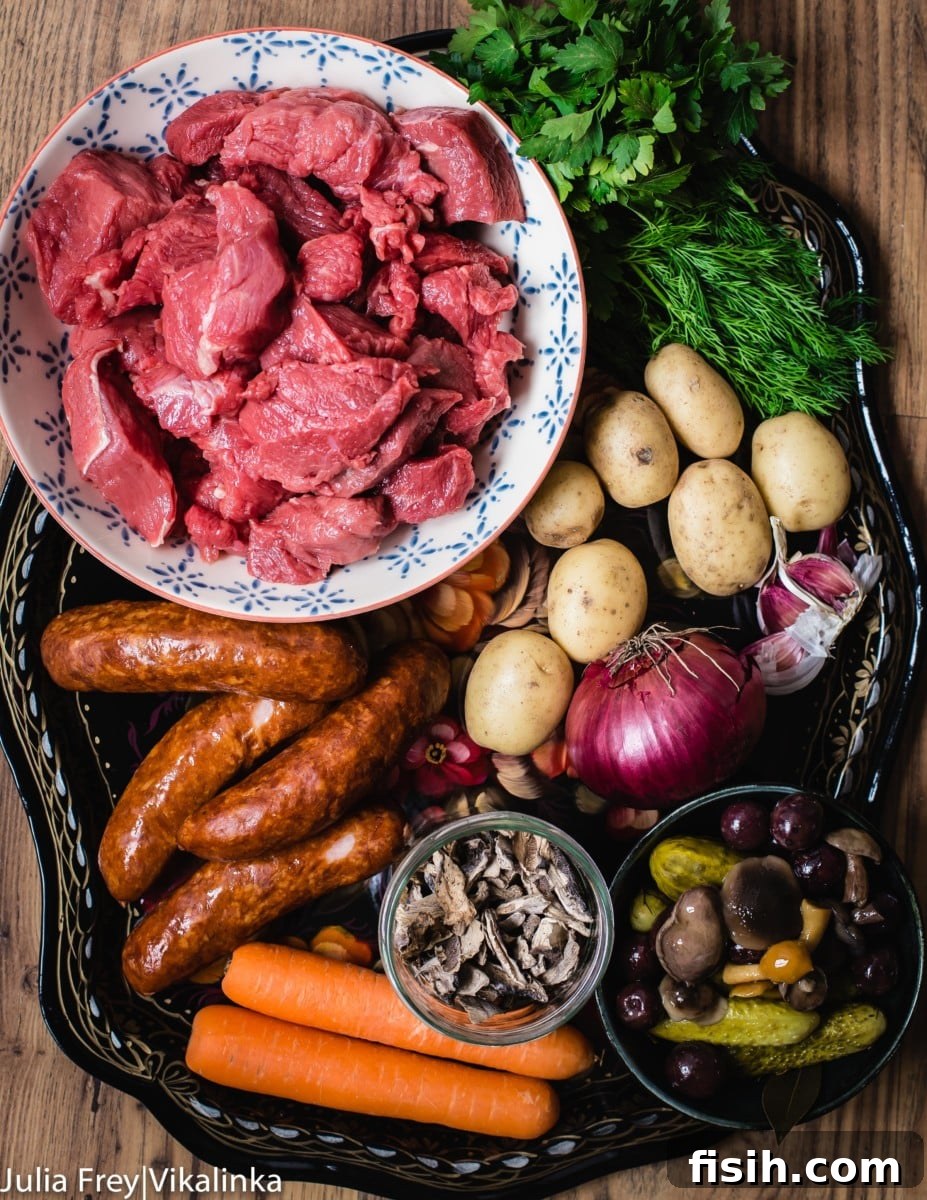 An array of fresh and preserved ingredients for Solyanka beef stew, including cubed beef, smoked sausage, bacon, various pickles, olives, and mushrooms, arranged neatly on a platter.