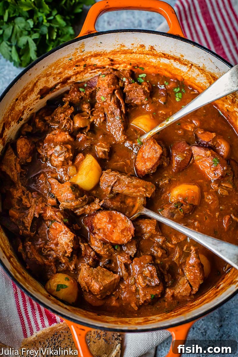 A close-up, top-down view of a rich Solyanka beef and sausage stew, bubbling gently in a rustic orange cast-iron pot, steam rising from its surface.
