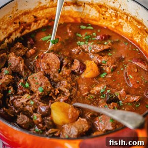 A rich, red-hued Russian beef solyanka stew simmering in a vibrant orange cast-iron pot, garnished with fresh herbs, ready to serve.