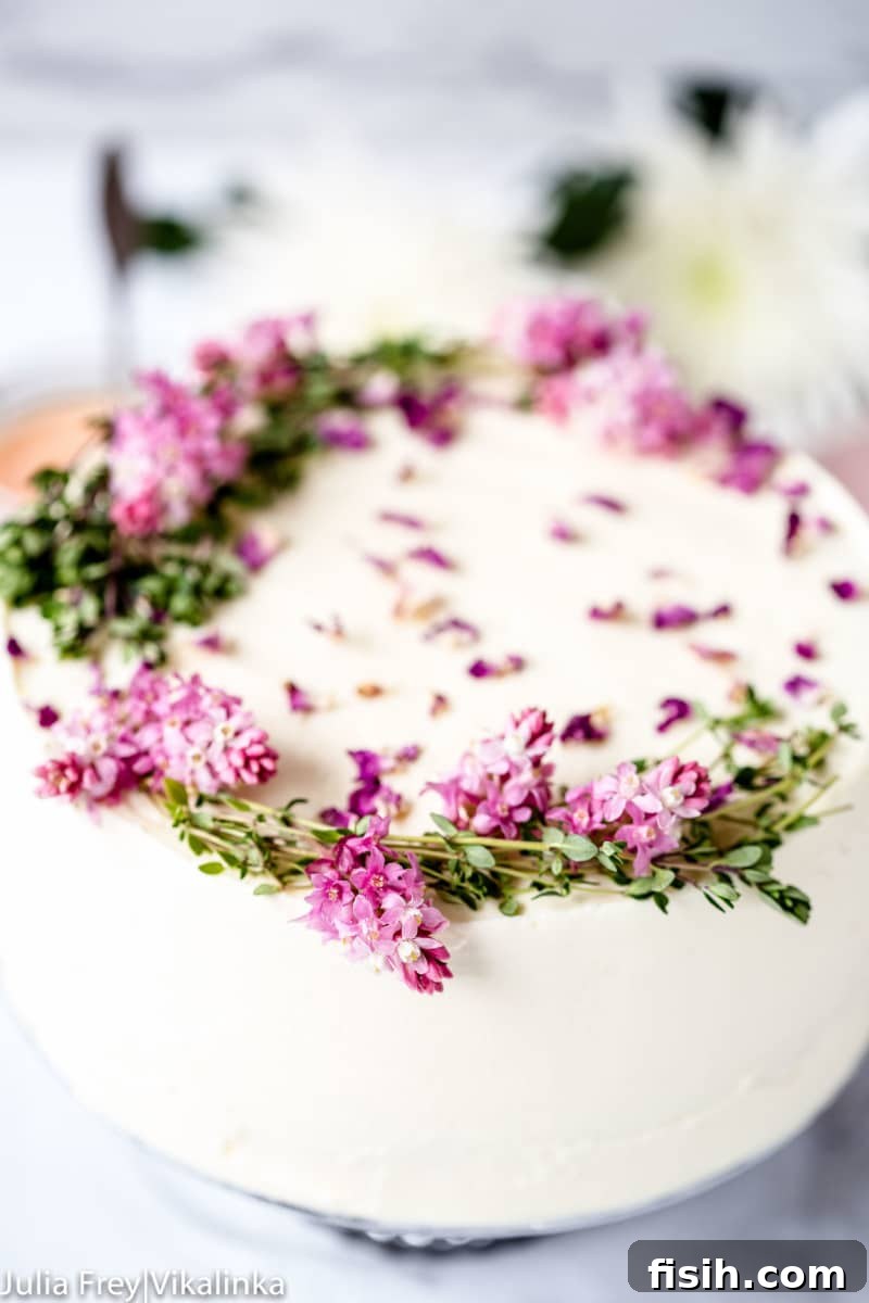 A beautifully frosted Rose Rhubarb Layer Cake, adorned with edible flowers and thyme, showcasing its delicate vanilla bean sponge and rich rhubarb curd filling.