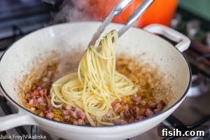 Tongs adding pasta to bacon