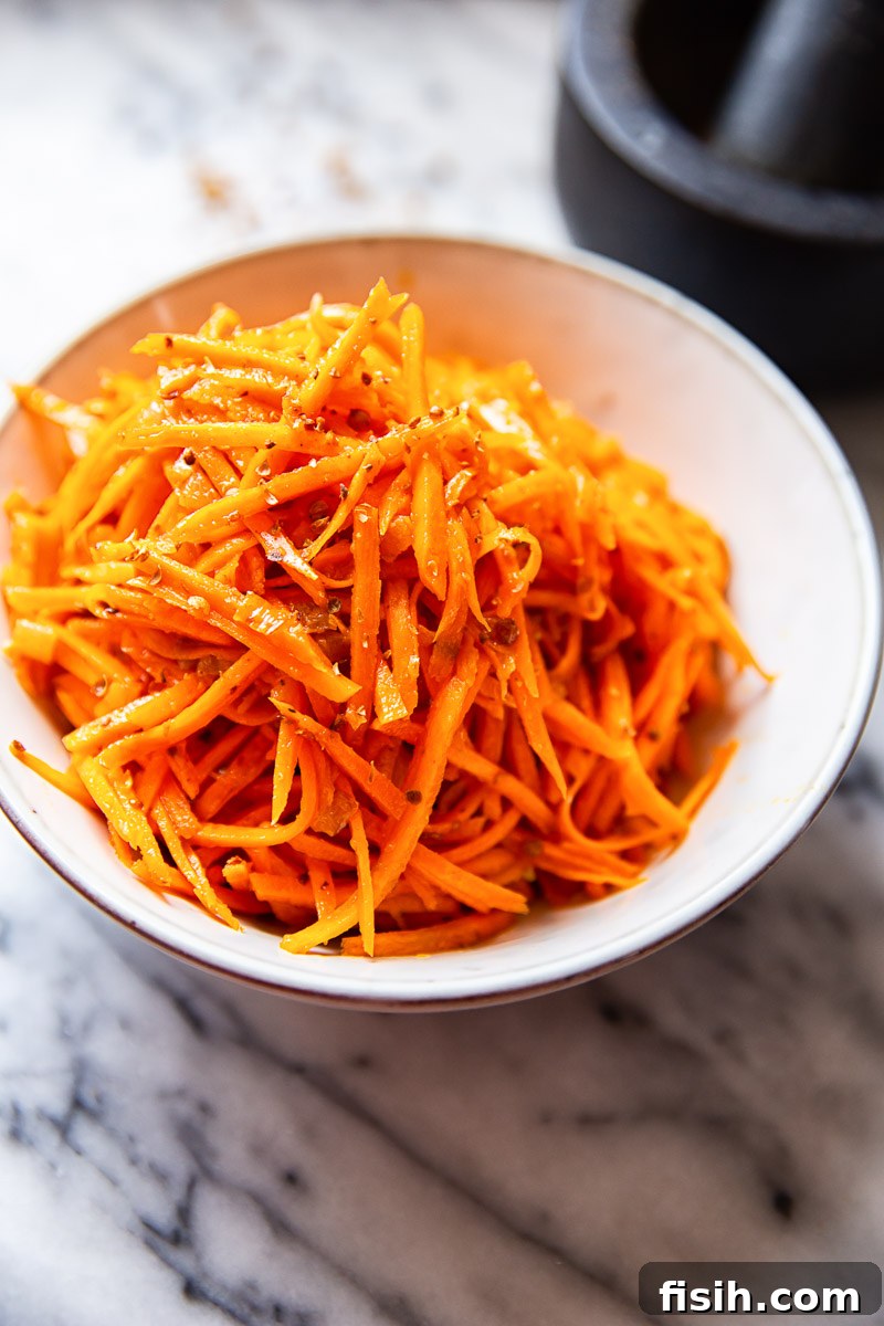 Spicy Korean Carrot Salad 2 Vibrant Korean Carrot Salad in a white bowl, showcasing julienned carrots and cracked coriander seeds.