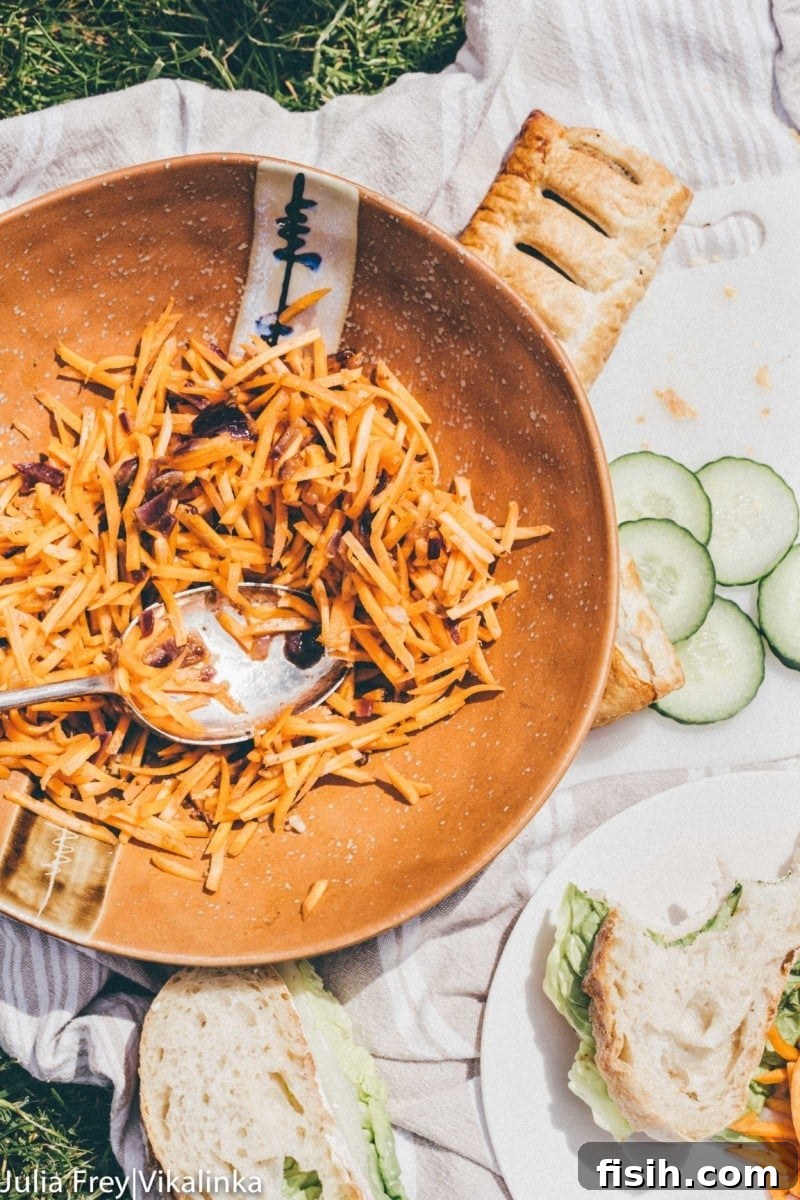 Spicy Korean Carrot Salad 4 A top-down view of a delightful picnic spread featuring sandwiches, fresh cucumber, and a bowl of vibrant Korean Carrot Salad.