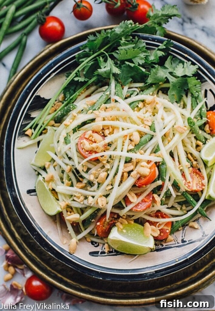 Top down view of a colorful Thai green papaya salad in a bowl, garnished with peanuts and lime wedges