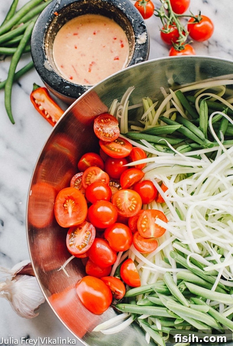 A mixing bowl filled with fresh salad ingredients including shredded papaya, green beans, and cherry tomatoes
