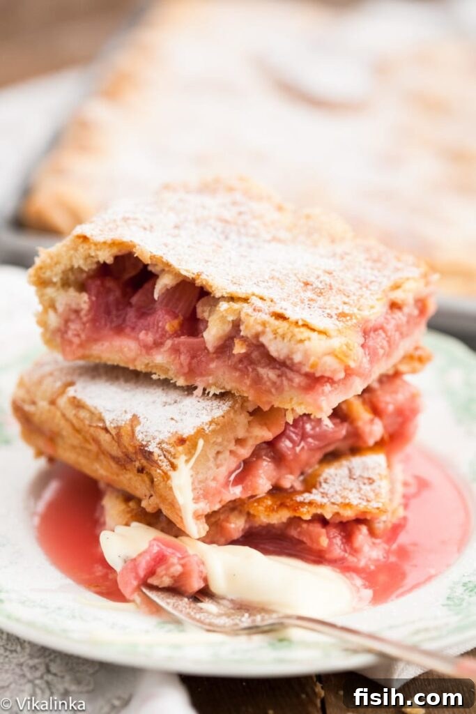 Generous Rhubarb Slab Pie 2 Close-up view of perfectly baked rhubarb slab pie slices stacked on a plate, highlighting the flaky crust and vibrant filling.
