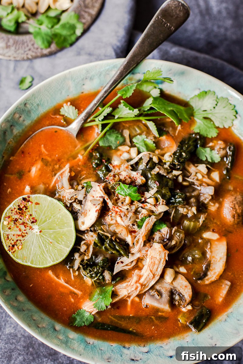 Creamy Coconut Thai Chicken and Rice Soup 3 top down view of Thai chicken and rice soup topped with sliced line and cilantro in a blue bowl.