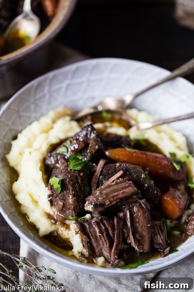A hearty bowl of Beef Bourguignon served over creamy mashed potatoes, with cutlery ready for a delicious meal.
