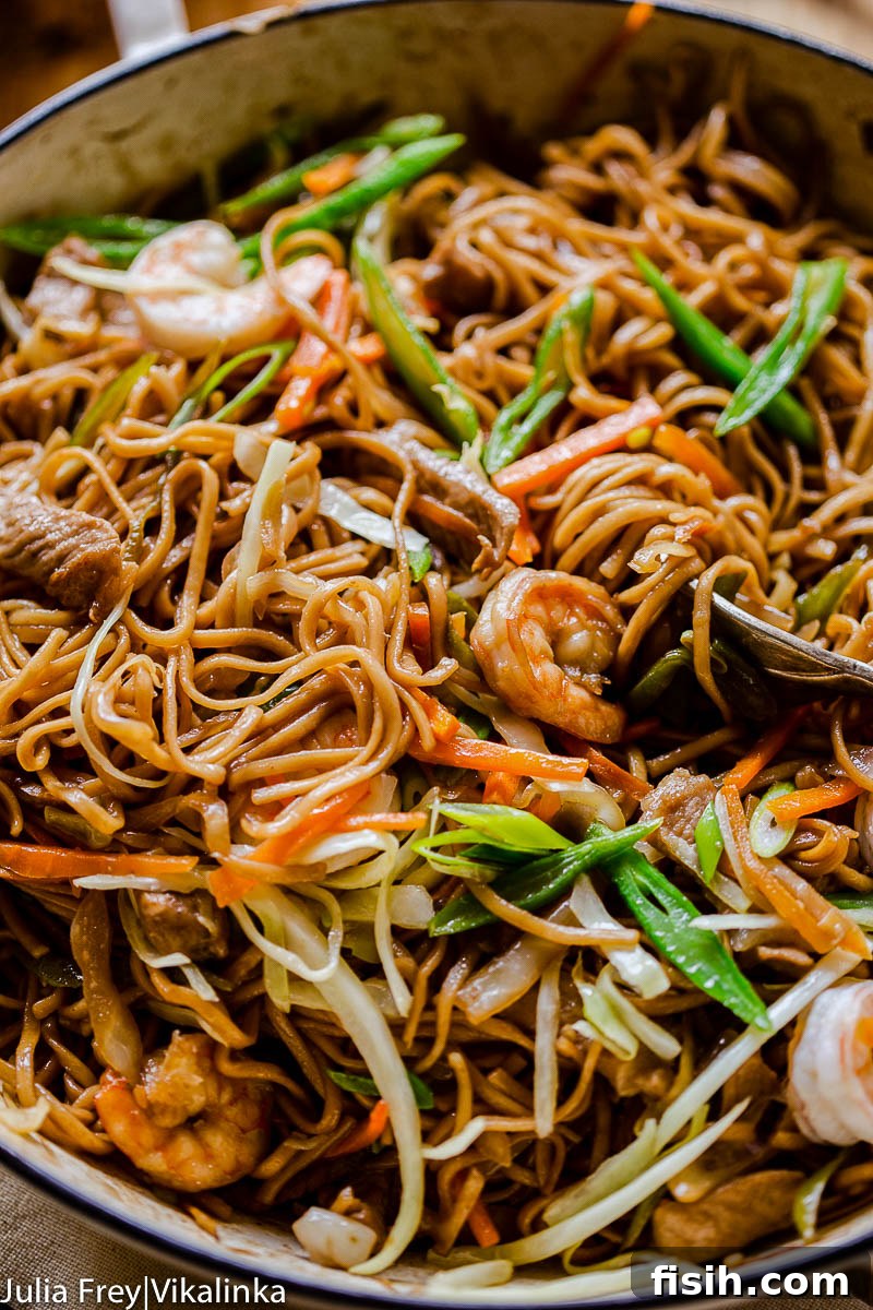 Flavorful stir-fried Pancit Canton noodles with green beans, carrots, tender pork, and shrimp, garnished with fresh herbs
