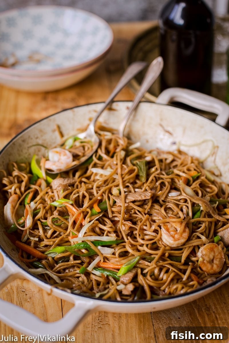 Pancit Canton served in a white pan, with additional bowls of noodles, shrimp, and vegetables in the background