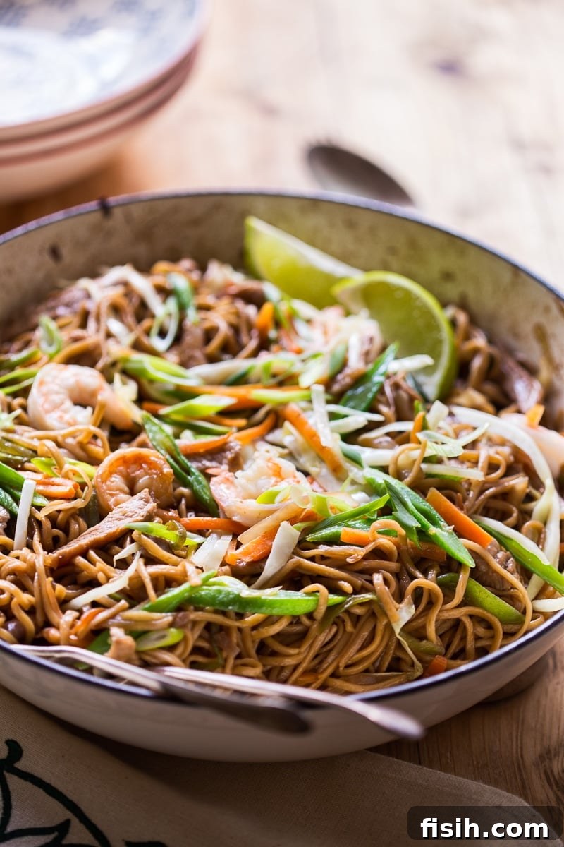 Pancit Canton cooking in a pan, showing noodles mixed with shrimp and vegetables (side view)