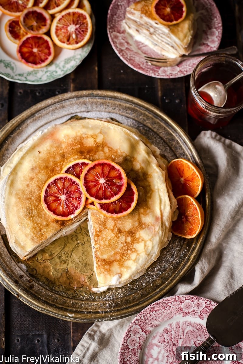 Top-down view of a completed blood orange ricotta crepe cake, garnished with fresh blood orange slices and powdered sugar