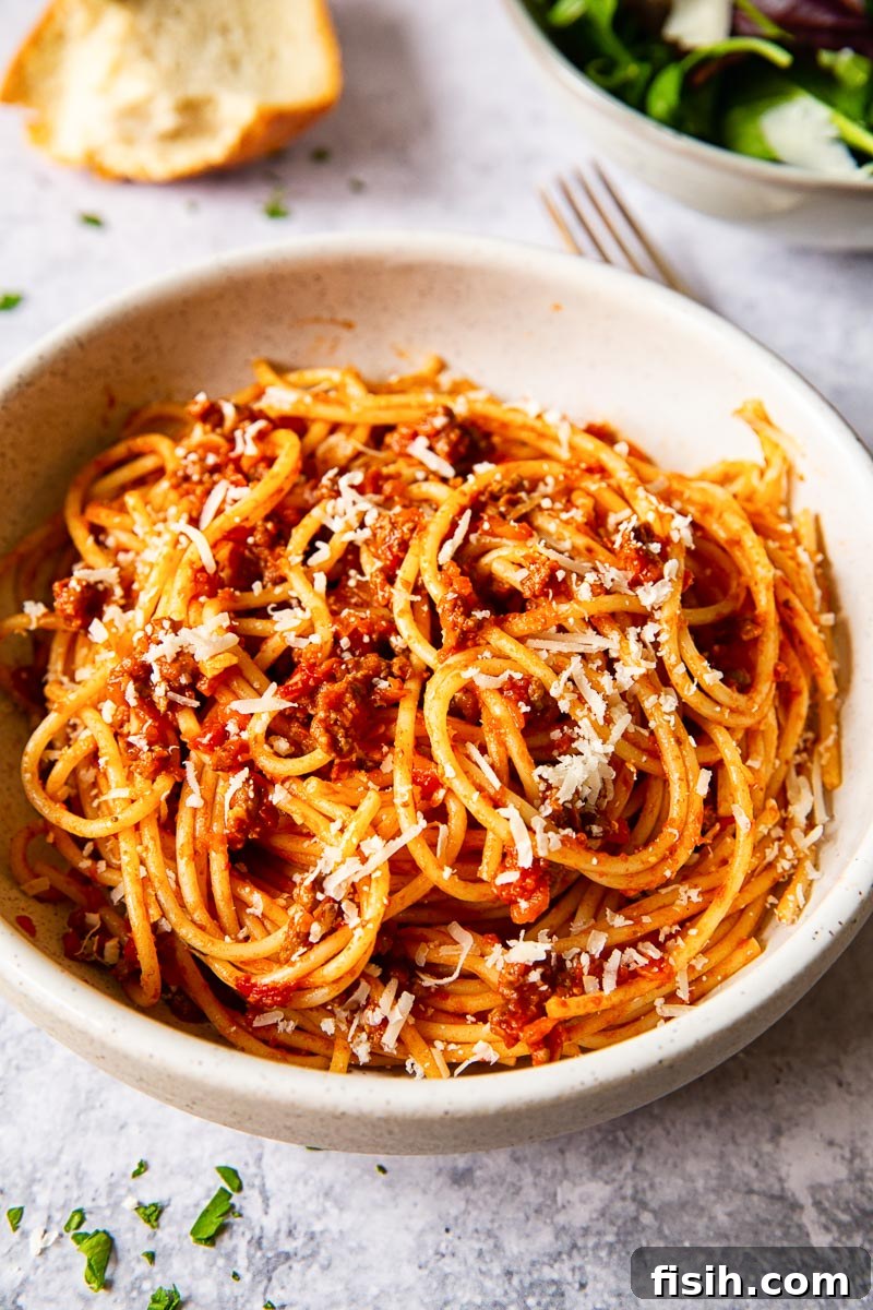Effortless Slow Cooker Bolognese 2 Classic spaghetti bolognese, generously sprinkled with Parmesan cheese, served in a creamy white bowl.