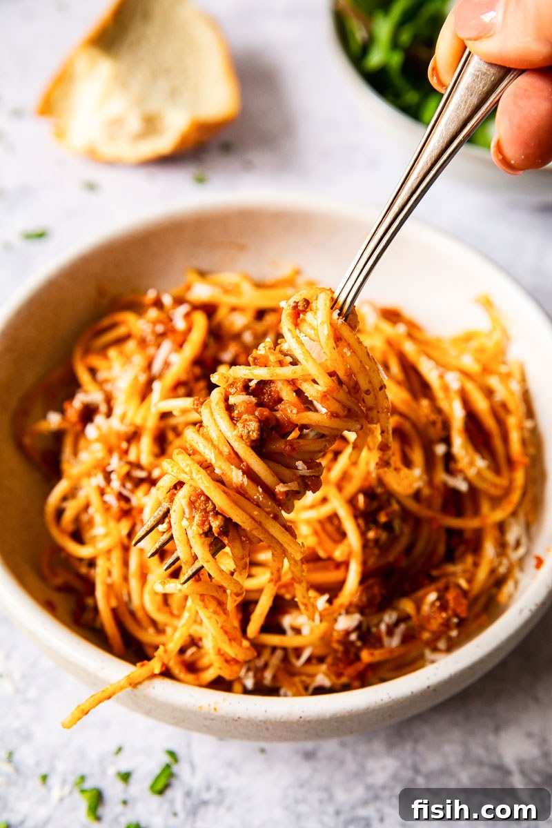 Effortless Slow Cooker Bolognese 4 Spaghetti expertly twirled around a fork, hovering over a bowl of rich bolognese sauce.