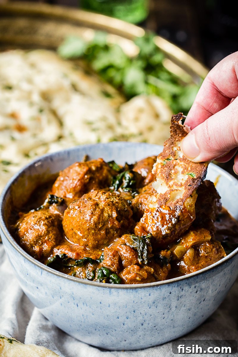 meatballs in a blue bowl and a hand dipping flatbread into the curry sauce